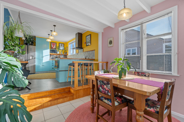 Dining area and kitchen with soft pink and bright yellow walls, and blue cabinetry.
