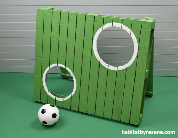 A painted wood pallet with holes in it with a soccer ball