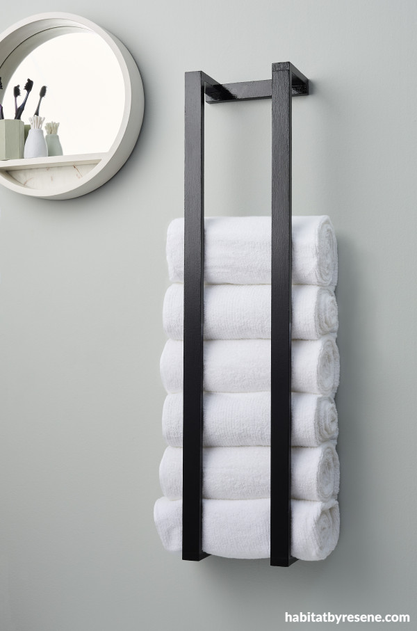 A glossy black towel holder on a blue wall with white towels