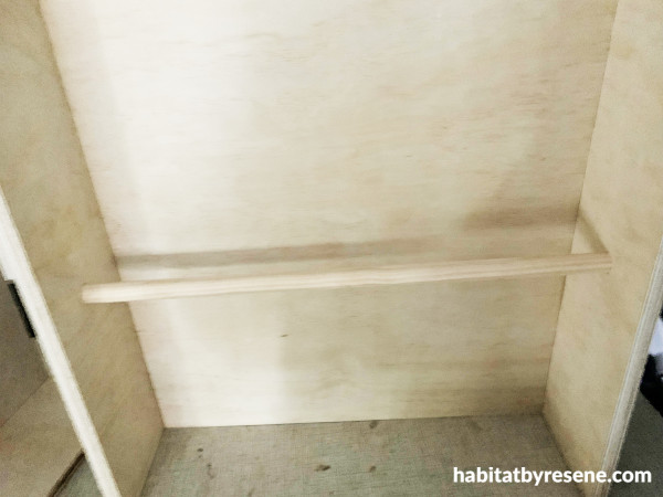 A wooden clothes rail attached to a wooden wardrobe top