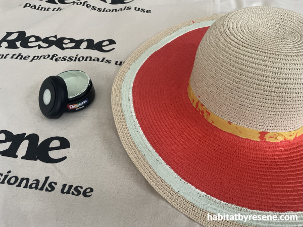 A hat painted in red with a green pot of paint next to it
