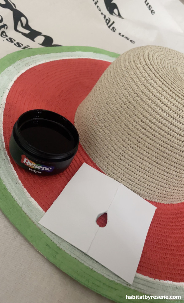 A hat painted in red, green and white with a black pot of paint and a piece of paper