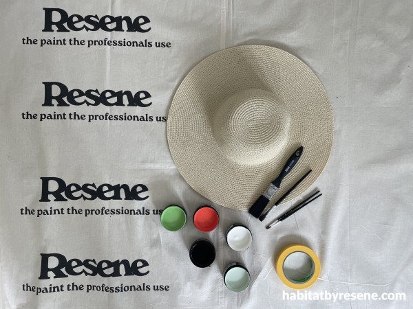 A hat, paint pots, paintbrushes and tape on a cloth