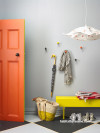 An entry with grey walls, orange door and yellow bench