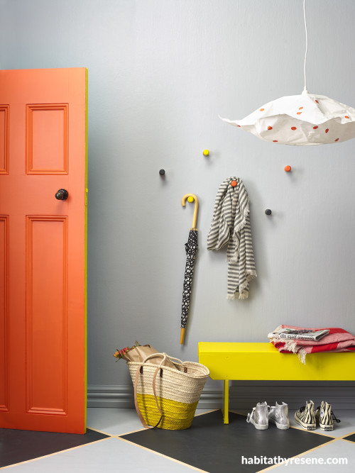 An entry with grey walls, orange door and yellow bench